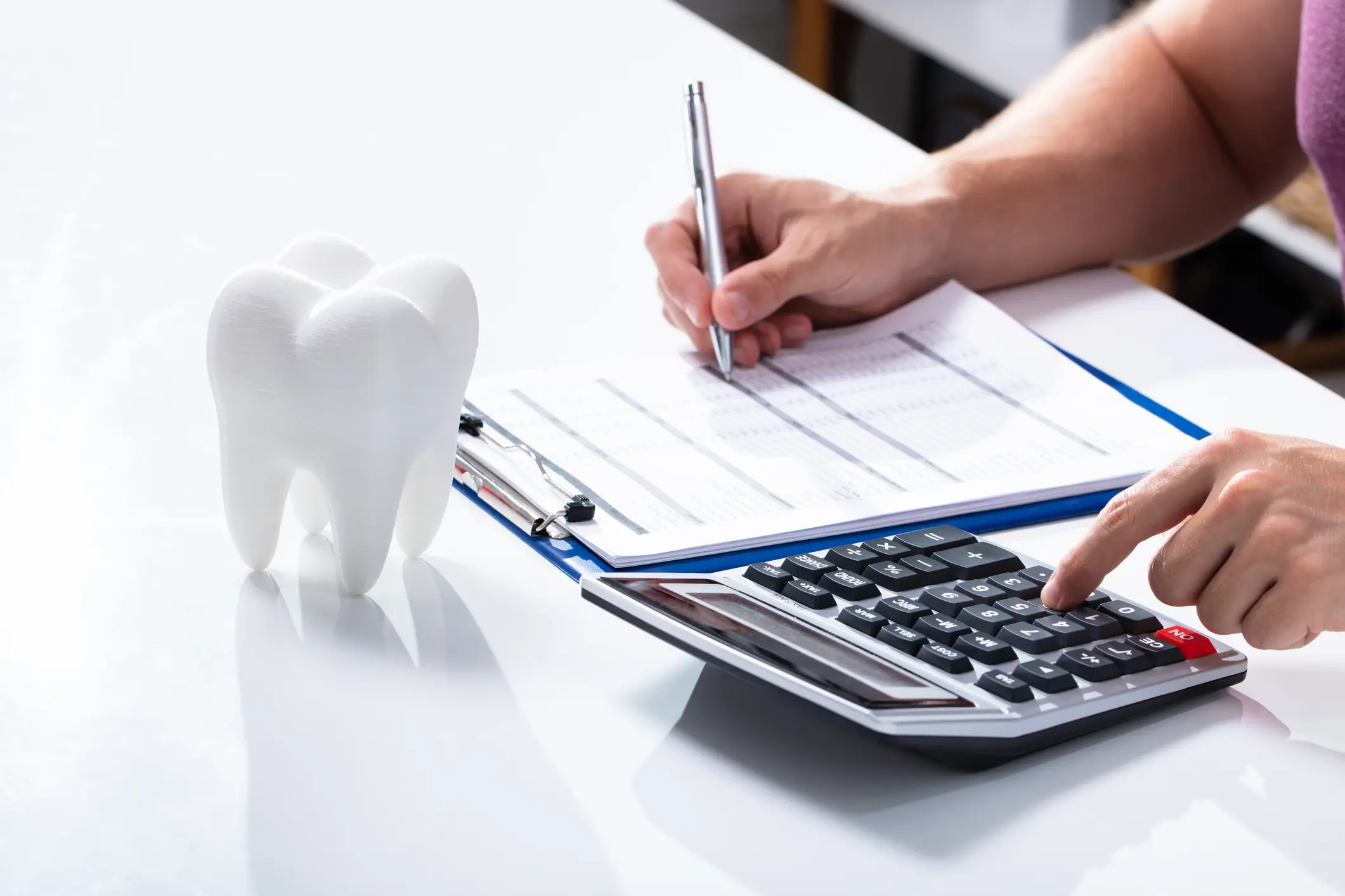 Close-up Of White Tooth Over Desk In Front Of Man Calculating Bill With Calculator